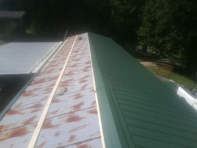 Old rusted panels beside newly installed green metal roofing — Wind Damage Roof Repair by Roofing Brothers in Crowley