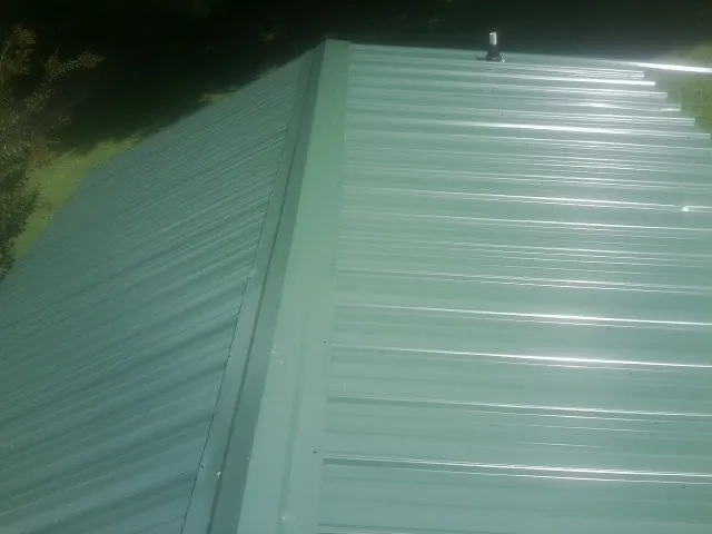 New green metal panels meeting at the ridge of a roof — Flat Roof Repair work by our crew in Crowley
