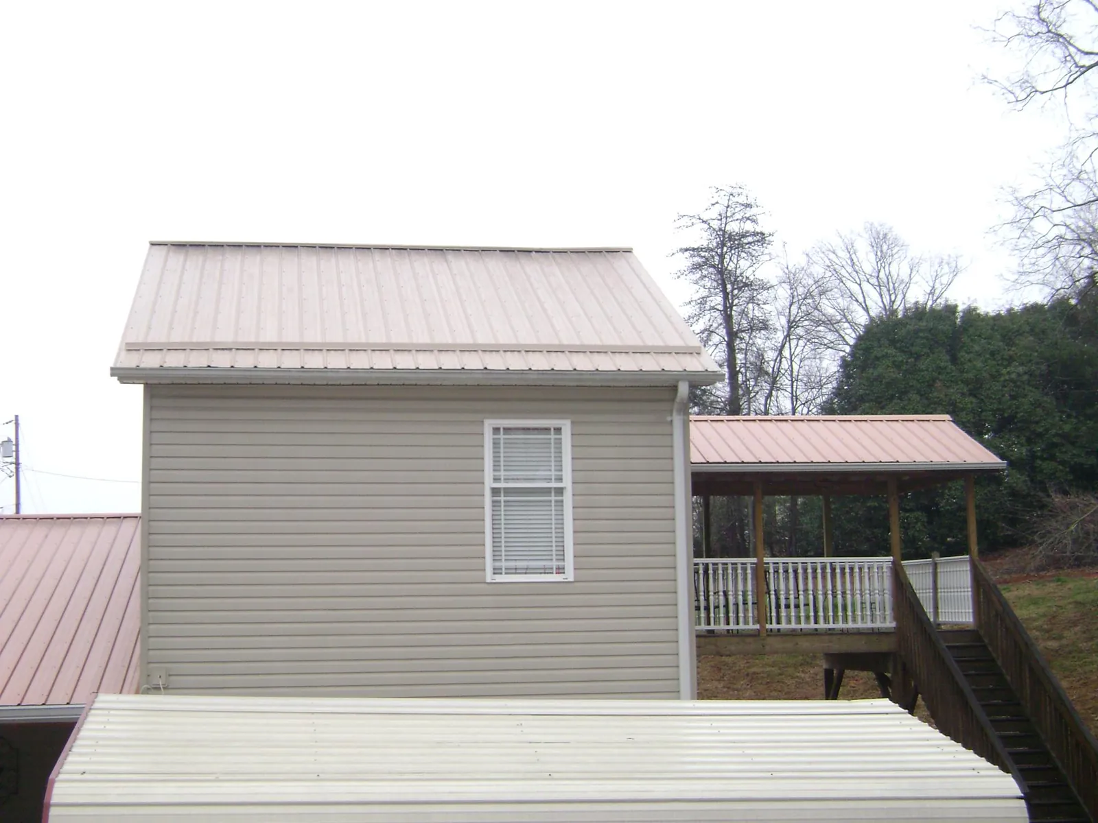 Tan metal roofs on a two story addition and attached porch, from a Roof Replacement job in Crowley