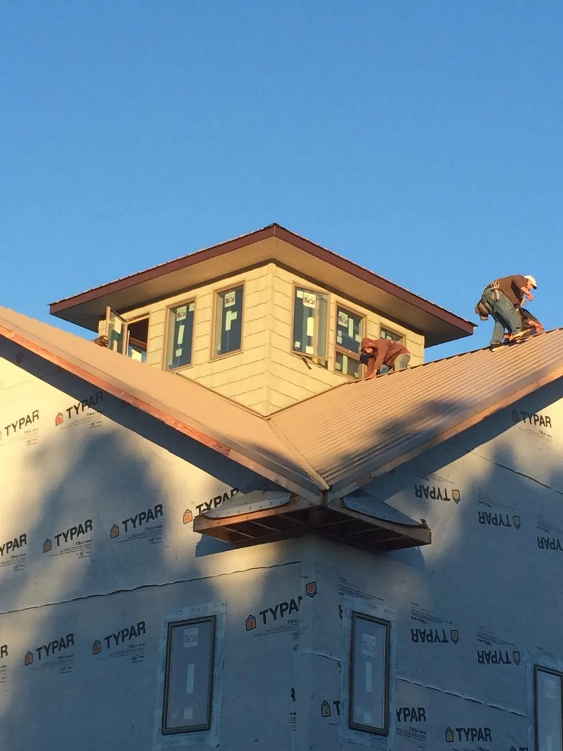 Roofers working around a rooftop cupola on a new metal roof at sunset — Roof Waterproofing in Crowley by Roofing Brothers